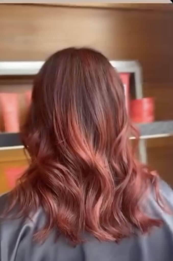 A person with medium-length, wavy, reddish-brown hair facing away from the camera, with shelves and red containers in the background.