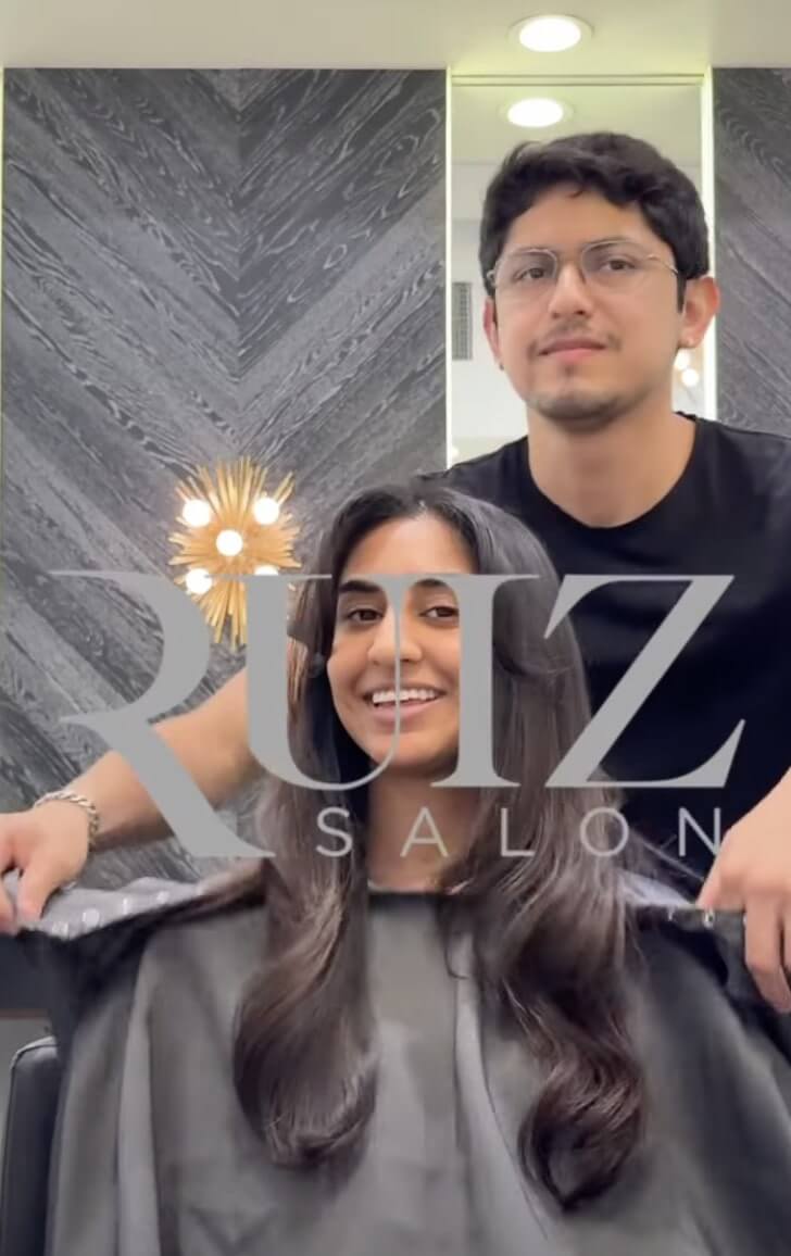 A woman with long, styled hair sits smiling in a salon chair, while a hairstylist stands behind her. The text "RUIZ SALON" is overlaid on the image.