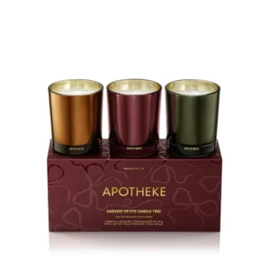 Three metallic-colored candles in glass holders are displayed on a maroon box labeled "Apotheke Harvest Petite Candle Trio.